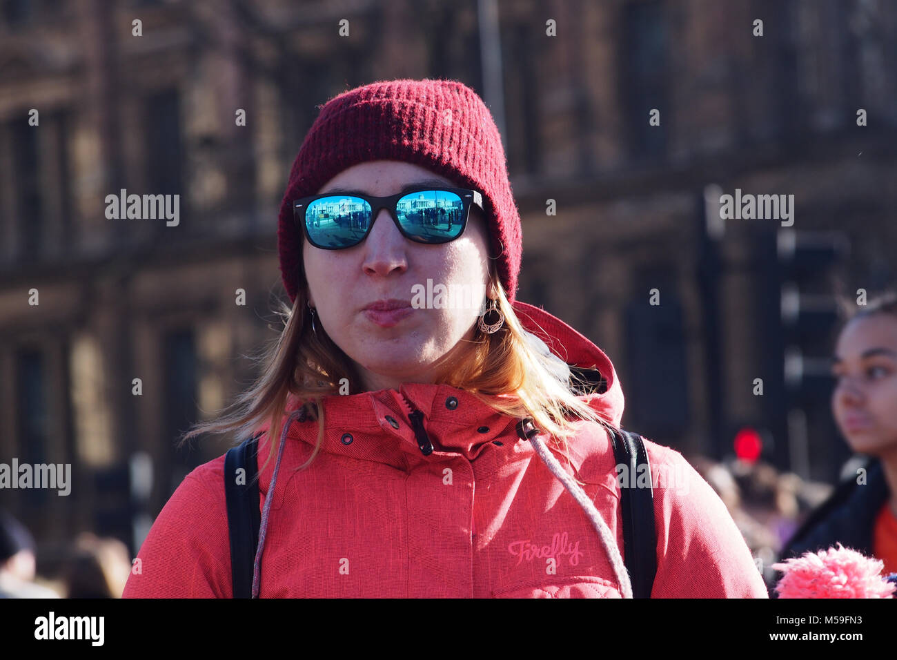 Eine Frau trägt einen roten Mantel mit Kapuze, eine Wollmütze und nachdenklich, Spiegel Sonnenbrille und Rucksack Stockfoto