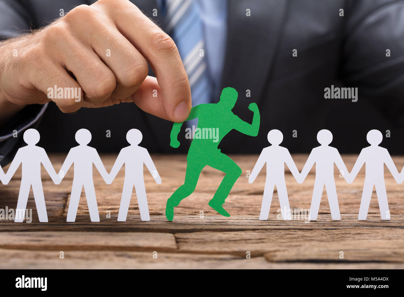 Mittelteil der Geschäftsmann holding Grün paperman läuft inmitten Team auf Tisch Stockfoto