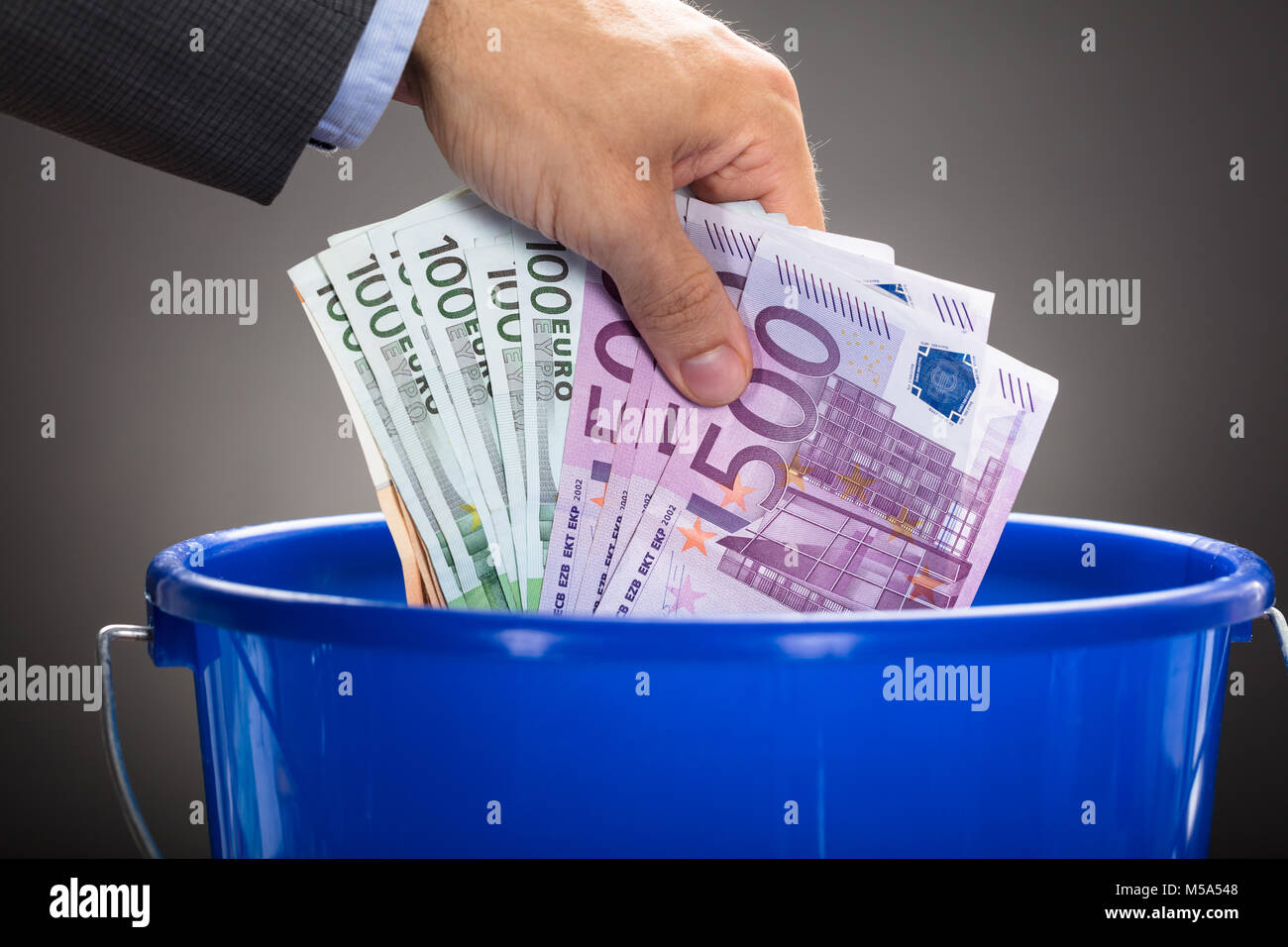 7/8 Hand des Kaufmanns werfen Euro-Banknoten in blau Schaufel gegen grauer Hintergrund Stockfoto