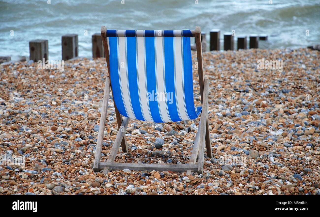 Ein einsamer blau-weiß gestreiften Liegestuhl am Strand in St. Leonards-on-Sea, East Sussex, England. Stockfoto