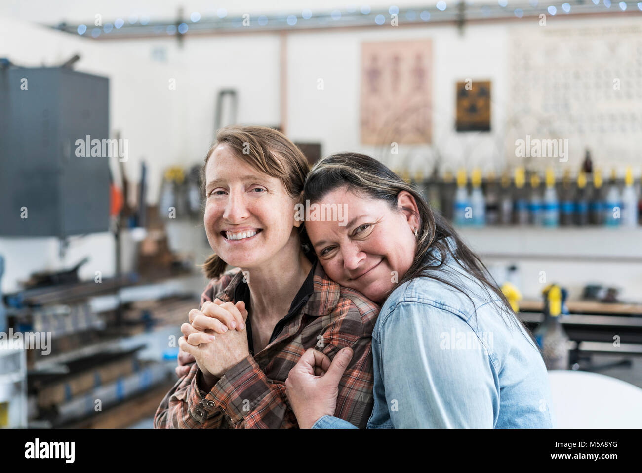 Zwei Frauen, die in der Metallwerkstatt, umarmen und lächelnd an der Kamera. Stockfoto