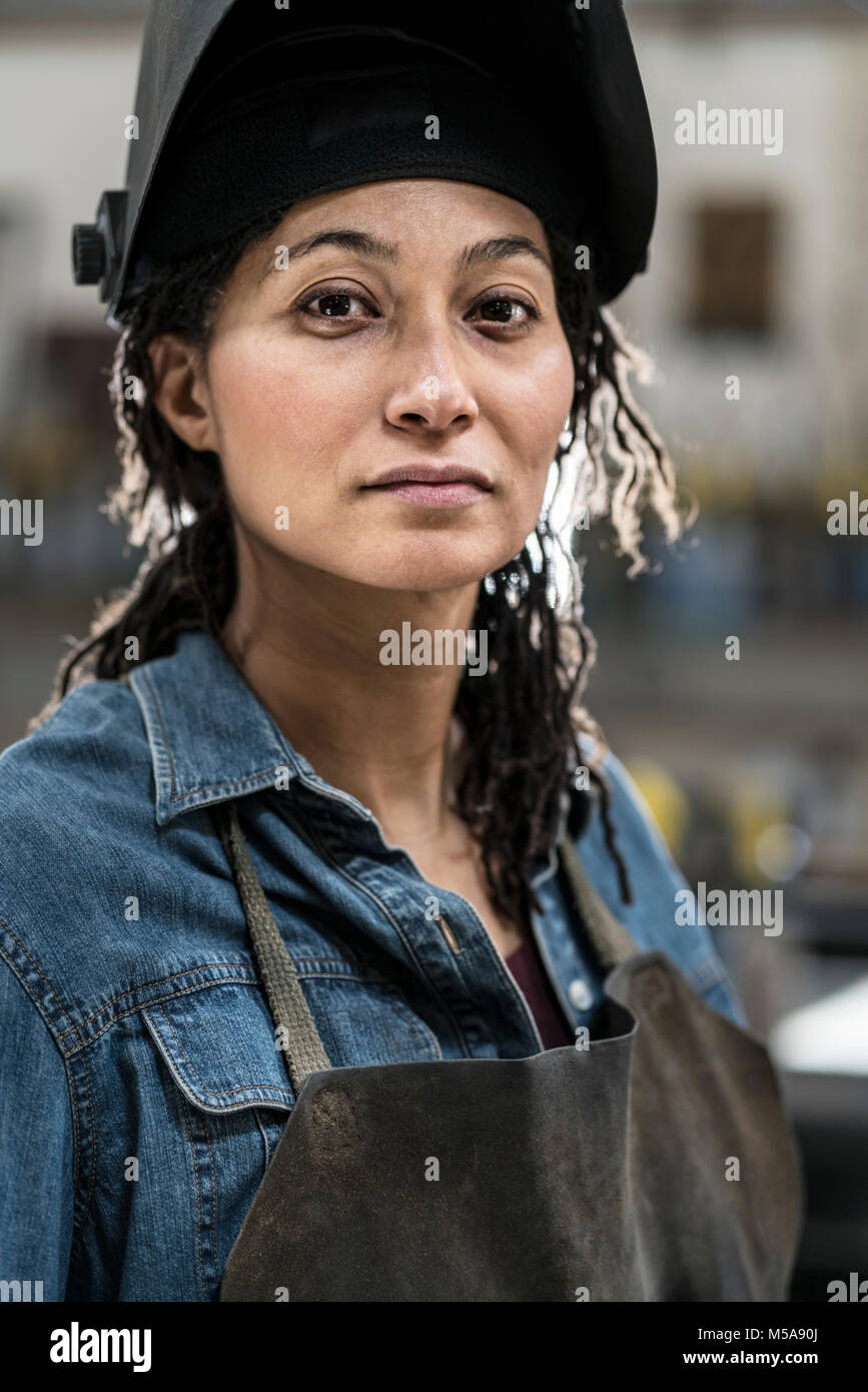 Portrait von Frau mit Schürze und schweißen Maske in der Metallwerkstatt, in die Kamera lächeln. Stockfoto