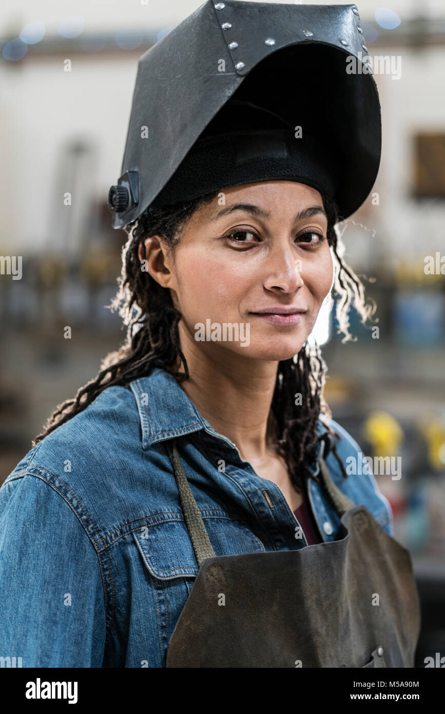 Portrait von Frau mit Schürze und schweißen Maske in der Metallwerkstatt, in die Kamera lächeln. Stockfoto