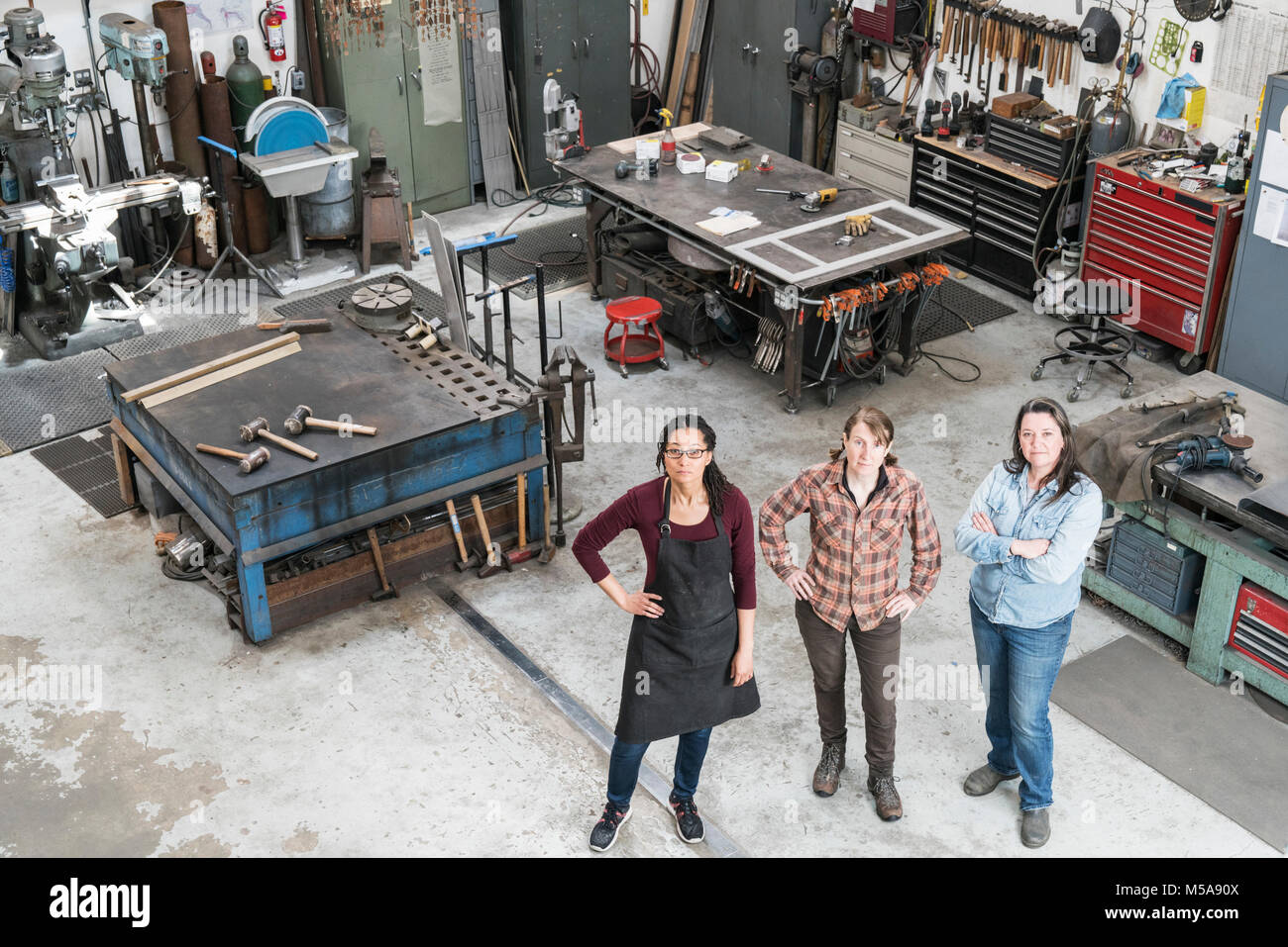 Hohe Betrachtungswinkel von drei Frauen, die in der Metallwerkstatt, an der Kamera schaut. Stockfoto