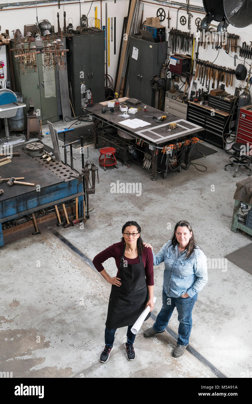 Hohe Betrachtungswinkel von zwei Frauen, die in der Metallwerkstatt, an der Kamera schaut. Stockfoto