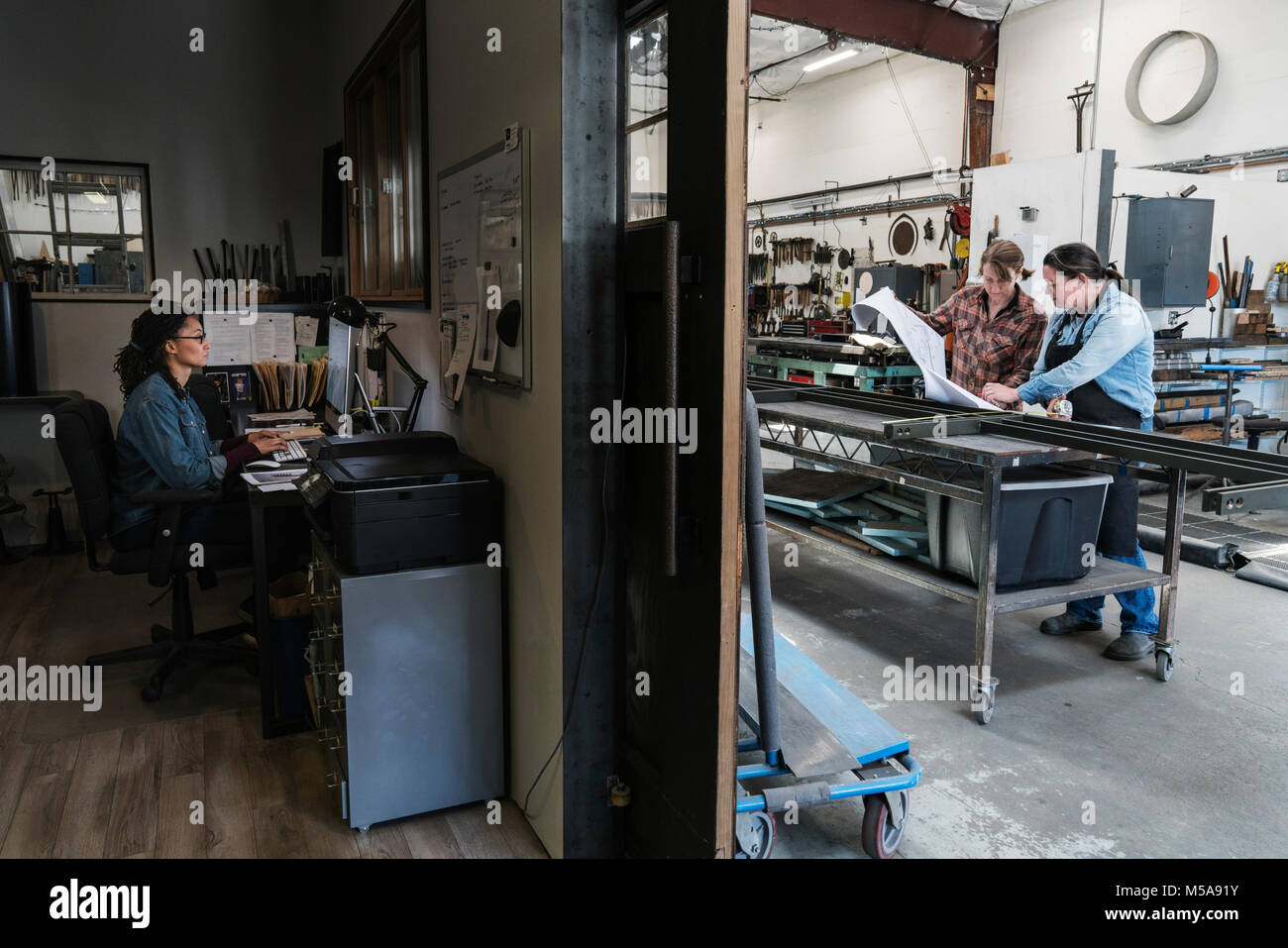 Zwei Frauen an einem Schreibtisch im Büro Bereich einer Metallwerkstatt, Frau, die auf dem mobile Werkbank. Stockfoto