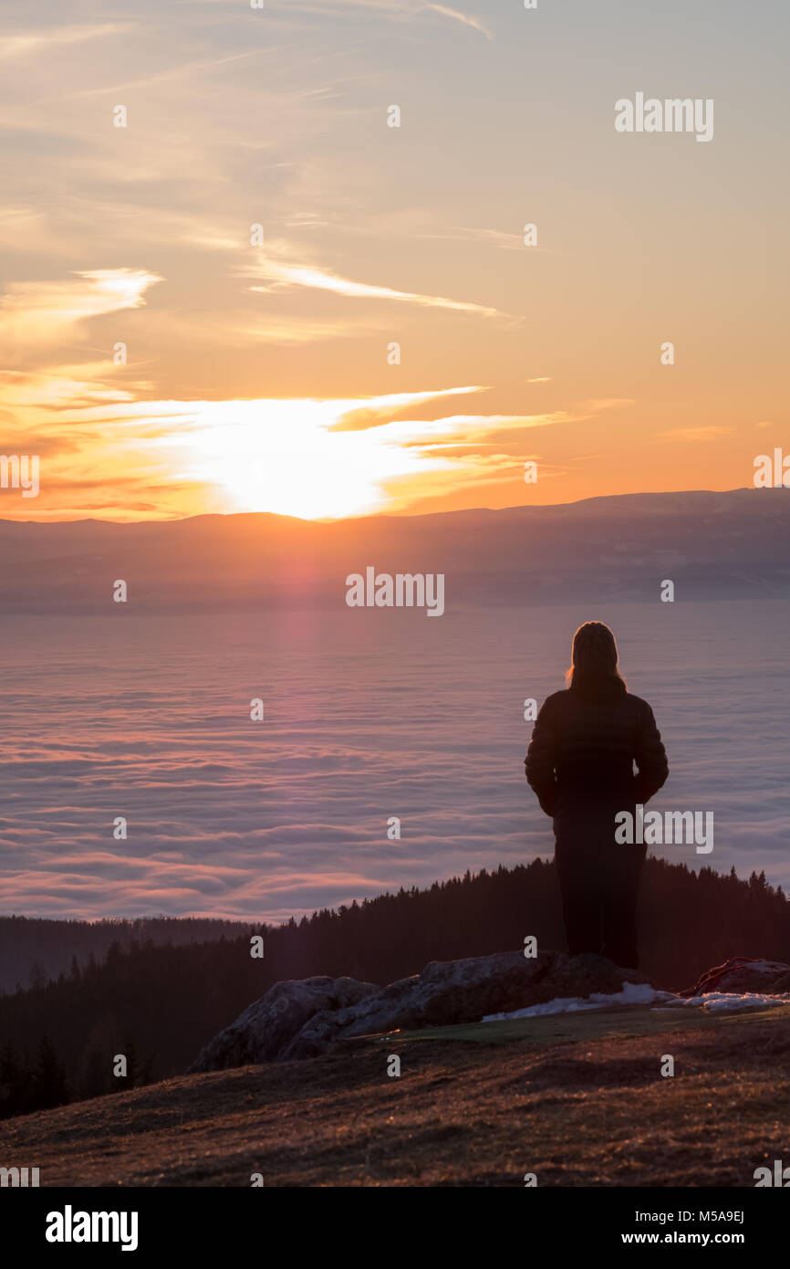Frau, die auf dem Gipfel des Berges Schoeckl in Österreich und Suchen über niedrige Stratus in der Stadt Graz zu Berg Koralpe bis Sonnenuntergang Stockfoto