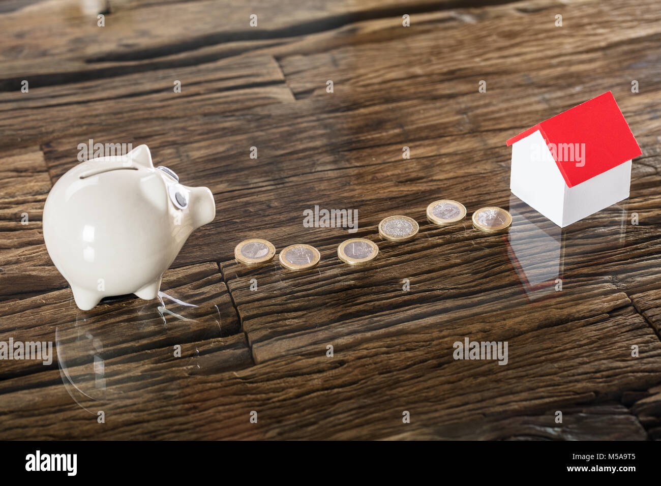 Euro Münzen zwischen den Sparschwein und Haus Modell auf hölzernen Schreibtisch Stockfoto