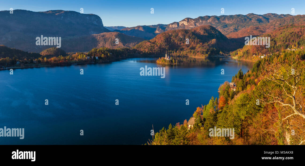 Bled, Slowenien - Panoramablick auf die Skyline Blick auf den Bleder See mit warmen Herbst Laub und die berühmte Wallfahrtskirche Mariä Himmelfahrt der Maria und die Alpen. Stockfoto