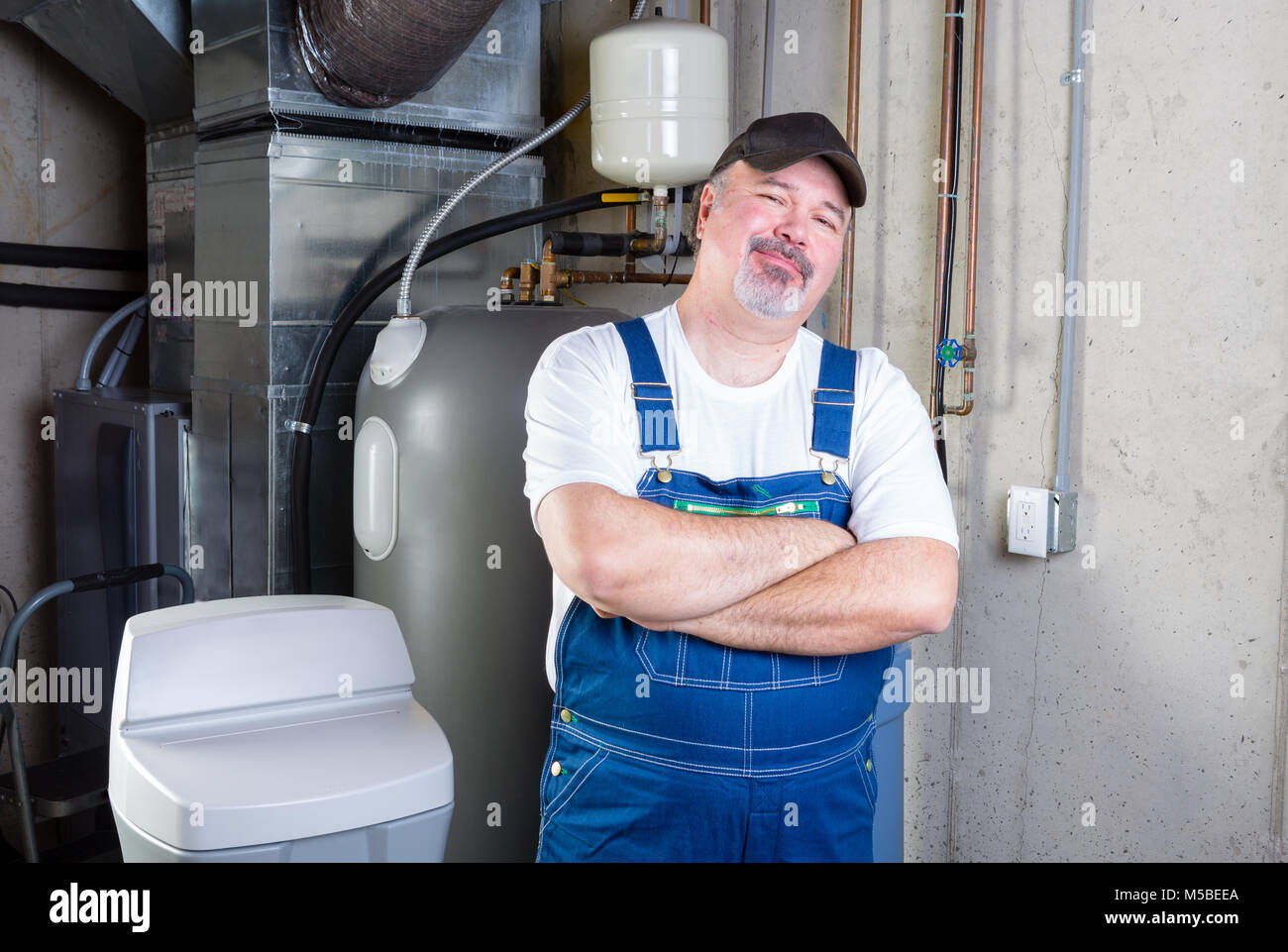 Zuversichtlich workman oder home Installer stehend in die Kamera lächelnd mit verschränkten Armen in einem Keller Abstellraum Stockfoto