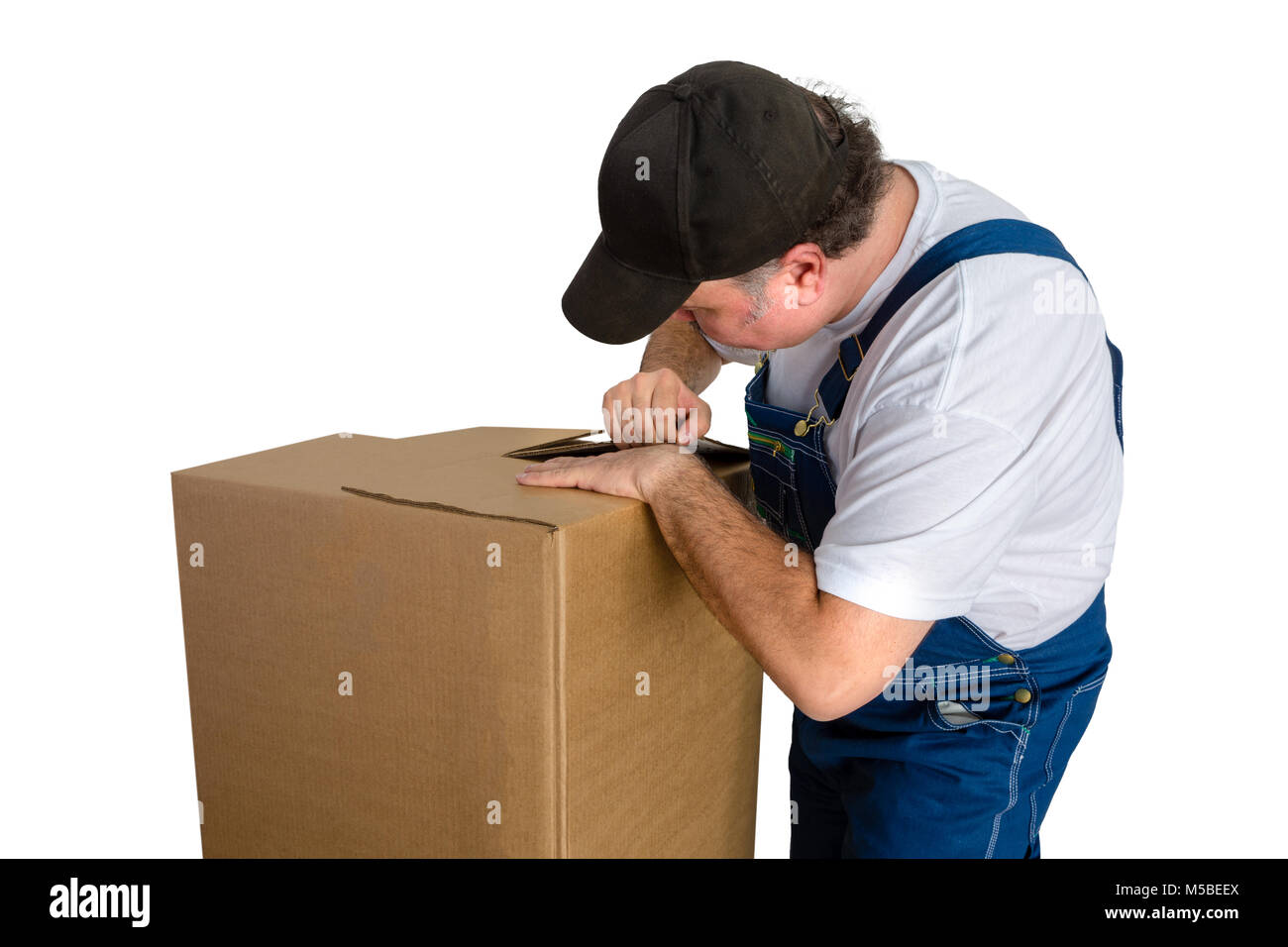 Männliche Arbeiter tragen Latzhose Eröffnung Karton vor weißem Hintergrund Stockfoto