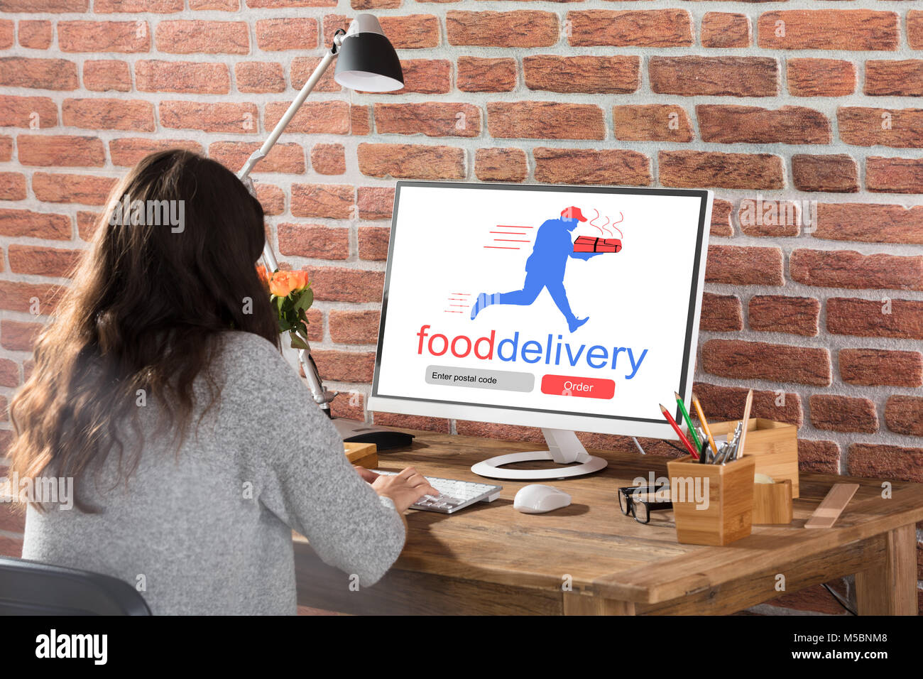 Ansicht der Rückseite eine Frau Essen bestellen Online am Computer am Arbeitsplatz Stockfoto