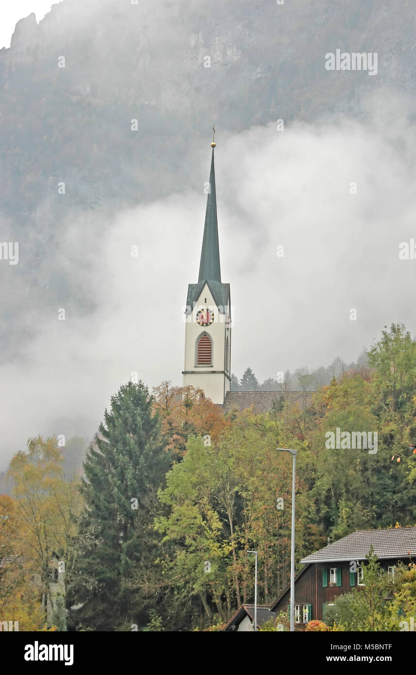 Eine typische hohe, elegante Dorfkirche Clock Tower in den Schweizer Alpen. Stockfoto