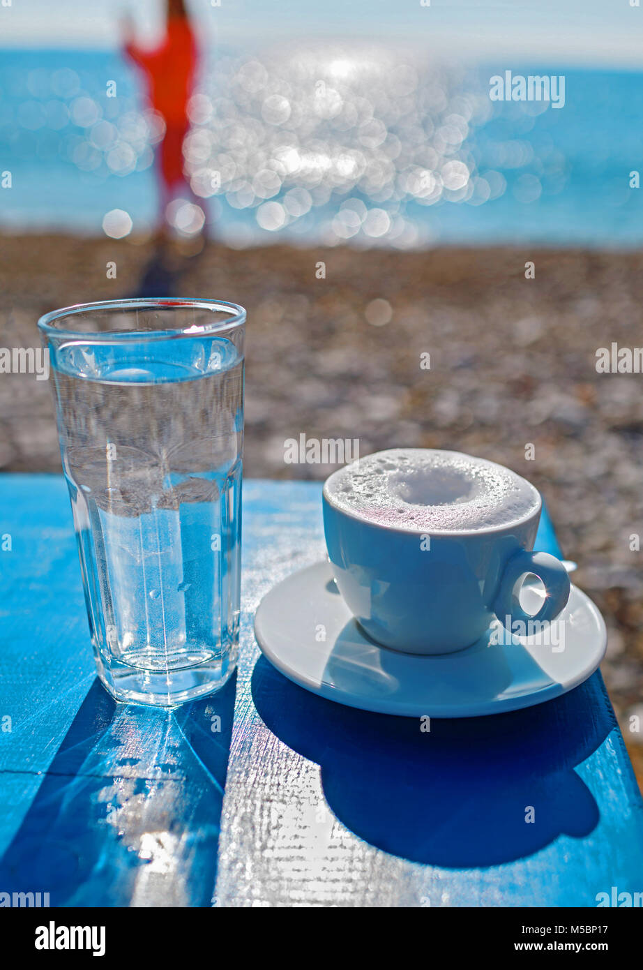 Tasse Kaffee oder Cappuccino auf dem blauen Tisch am Strand. Sommer Entspannung am Strand. Stockfoto