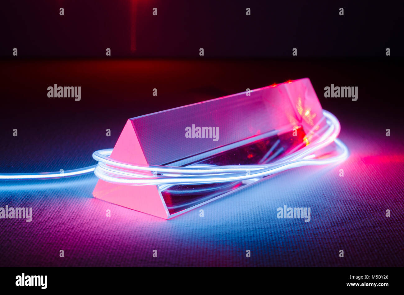 Ein Studio Still life Foto von einem dreieckigen Glasprisma mit abstrakten Neon Beleuchtung in Blau-grau, und rotes Laserlicht in das Ende des Prisma Stockfoto