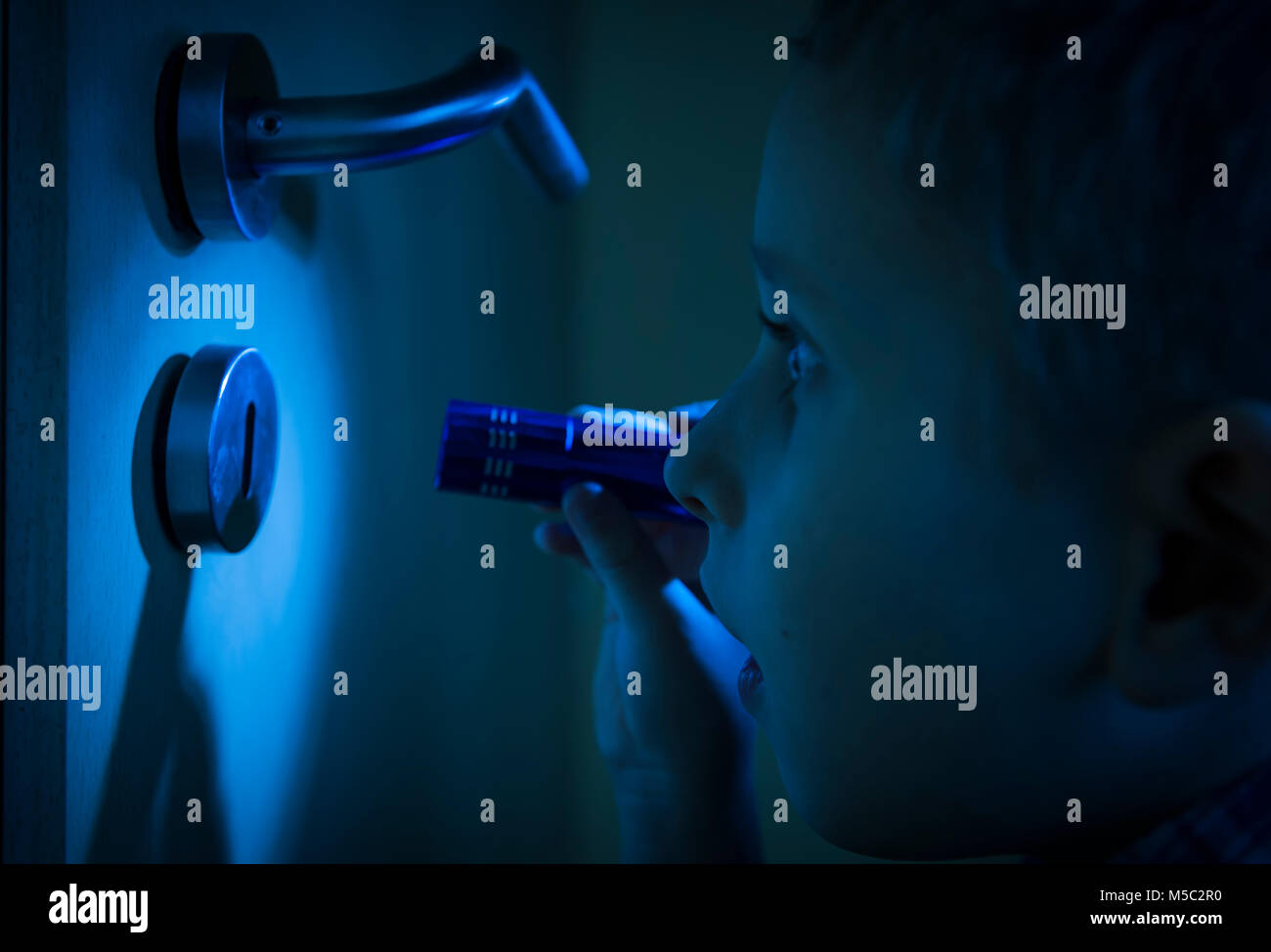 Junge im dunklen Zimmer blickt im Schein der Taschenlampe durch ein Schlüsselloch. Stockfoto