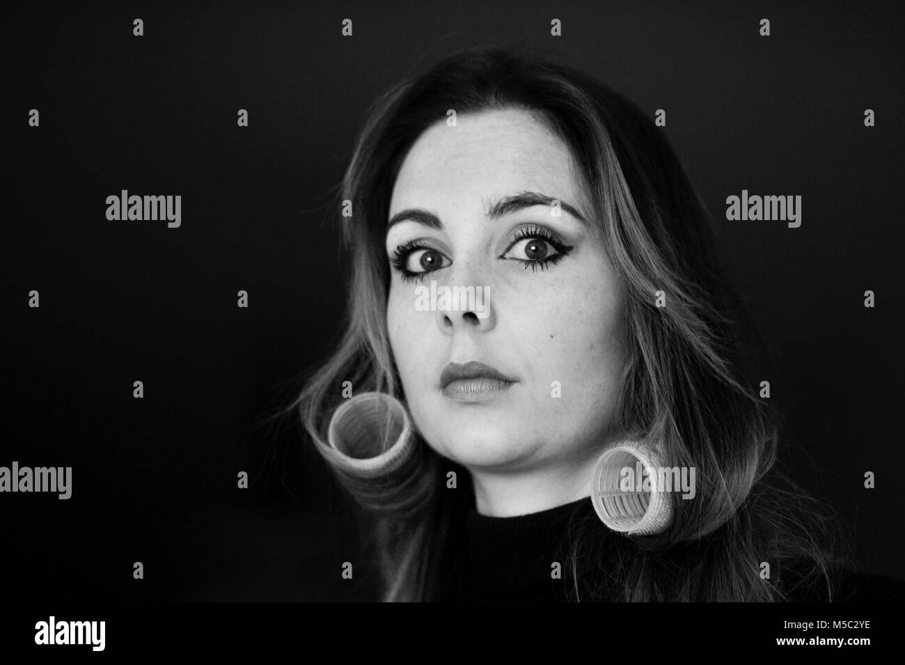 Schöne junge Frau mit Brünette Haar Haar Rollen gegen den dunklen Hintergrund Stockfoto