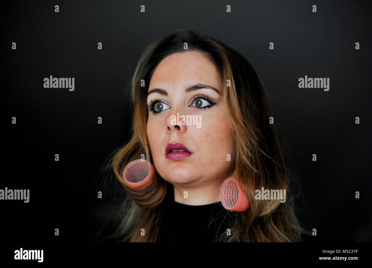 Schöne junge Frau mit Brünette Haar Haar Rollen gegen den dunklen Hintergrund Stockfoto