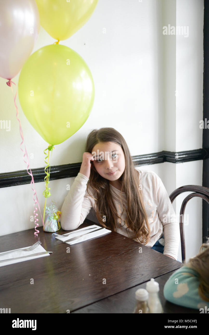 Ein einsames kleines Mädchen sitzt an einem eingerichteten party Tisch und schaut nachdenklich und traurig Stockfoto