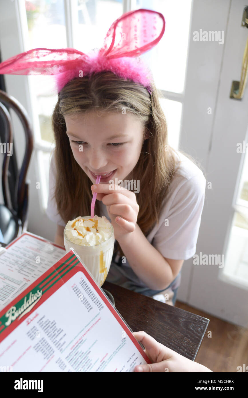 Hübsches Mädchen trinken einen Milchshake in einem Cafe tragen eine große rosa Schleife im Haar. Stockfoto