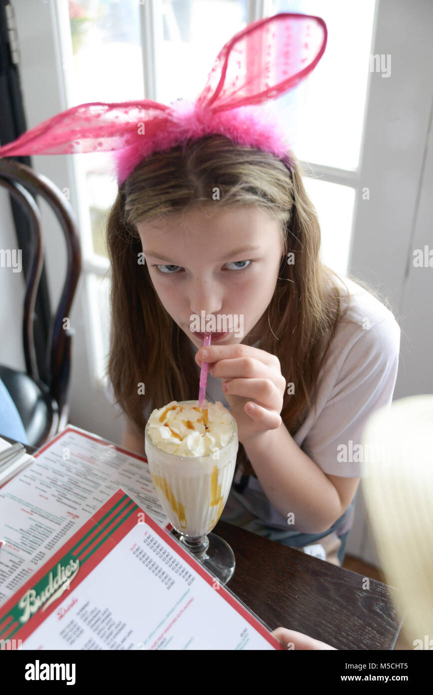 Hübsches Mädchen trinken einen Milchshake in einem Cafe tragen eine große rosa Schleife im Haar. Stockfoto