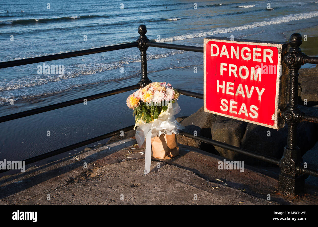 Die Blumen liegen als Zeichen der Erinnerung für jemanden, der in schwerer See ertrunken. Der Hinweis warnt andere vor den Gefahren. Stockfoto