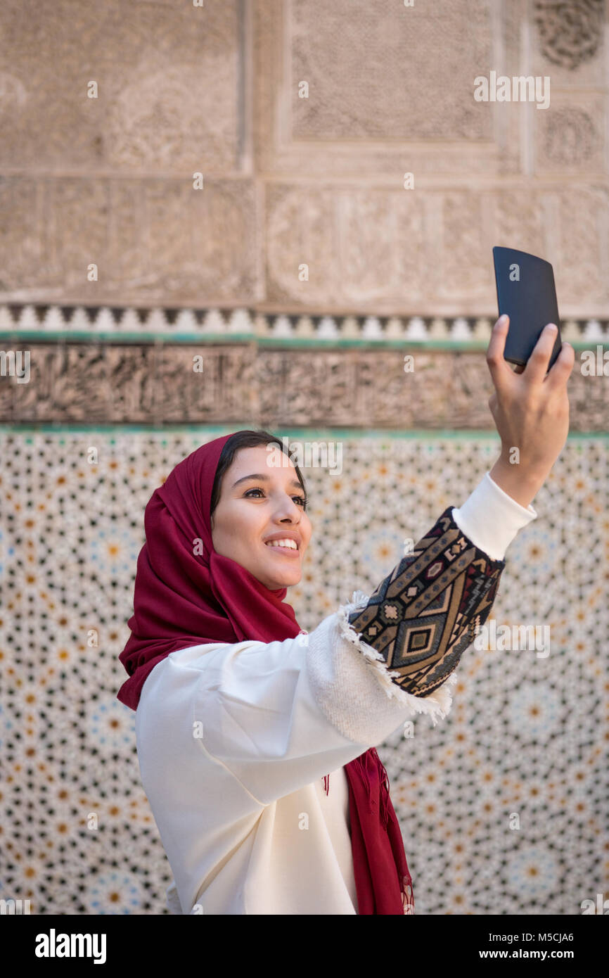 Muslimische Frau unter selfie mit Handy in traditioneller Kleidung mit roten Kopftuch auf dem Kopf Stockfoto