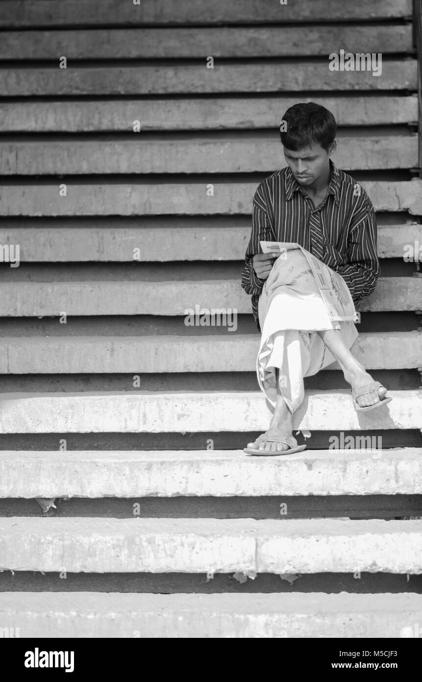 Mann lesen Zeitung an den Treppen von einer Brücke bei Dhaka Bahnhof Stockfoto