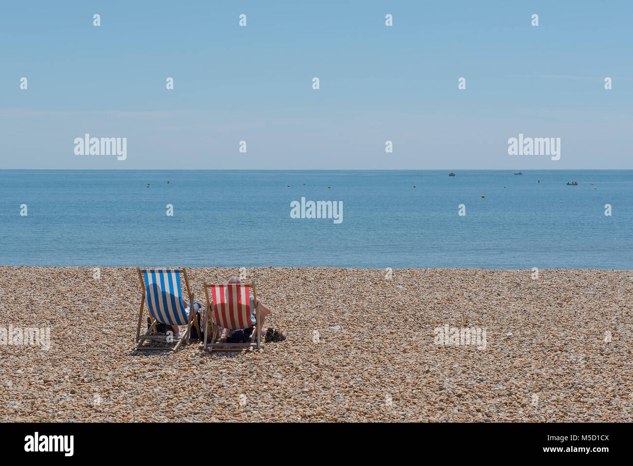 Die steigenden Temperaturen an der Südküste von England als Paar entspannen Sie sich auf traditionelle gestreifte Liegestühle mit Sonnenschirm auf einem glühend heißen Tag in Lyme Regis Stockfoto
