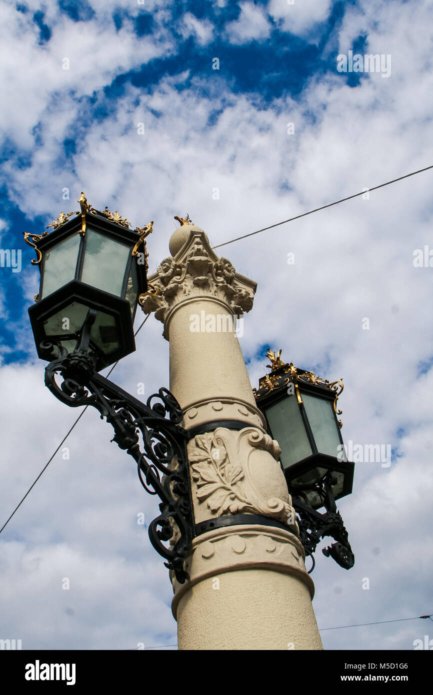 Alter - altes Eisen Spitze Stadt Straße Licht auf Stein pole gegen den blauen Himmel und weißen Wolken Cumulus in alte europäische Stadt Stockfoto