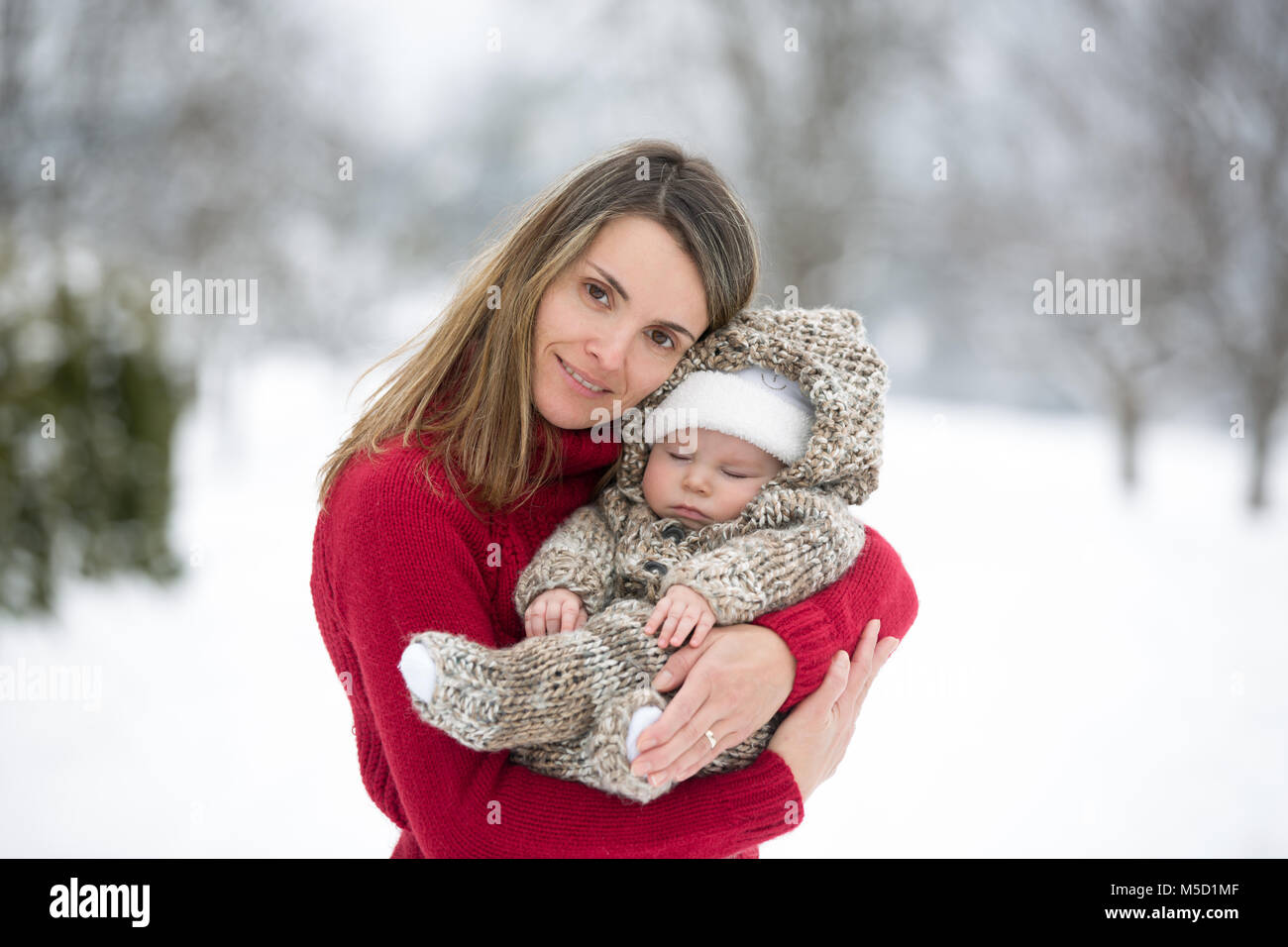 Schönen Mutter und niedlichen Baby boy in gestrickt, Body, mit ihren schönen Winter Outdoor Portrait auf einer sonnigen Winter schneebedeckten Tag genommen Stockfoto