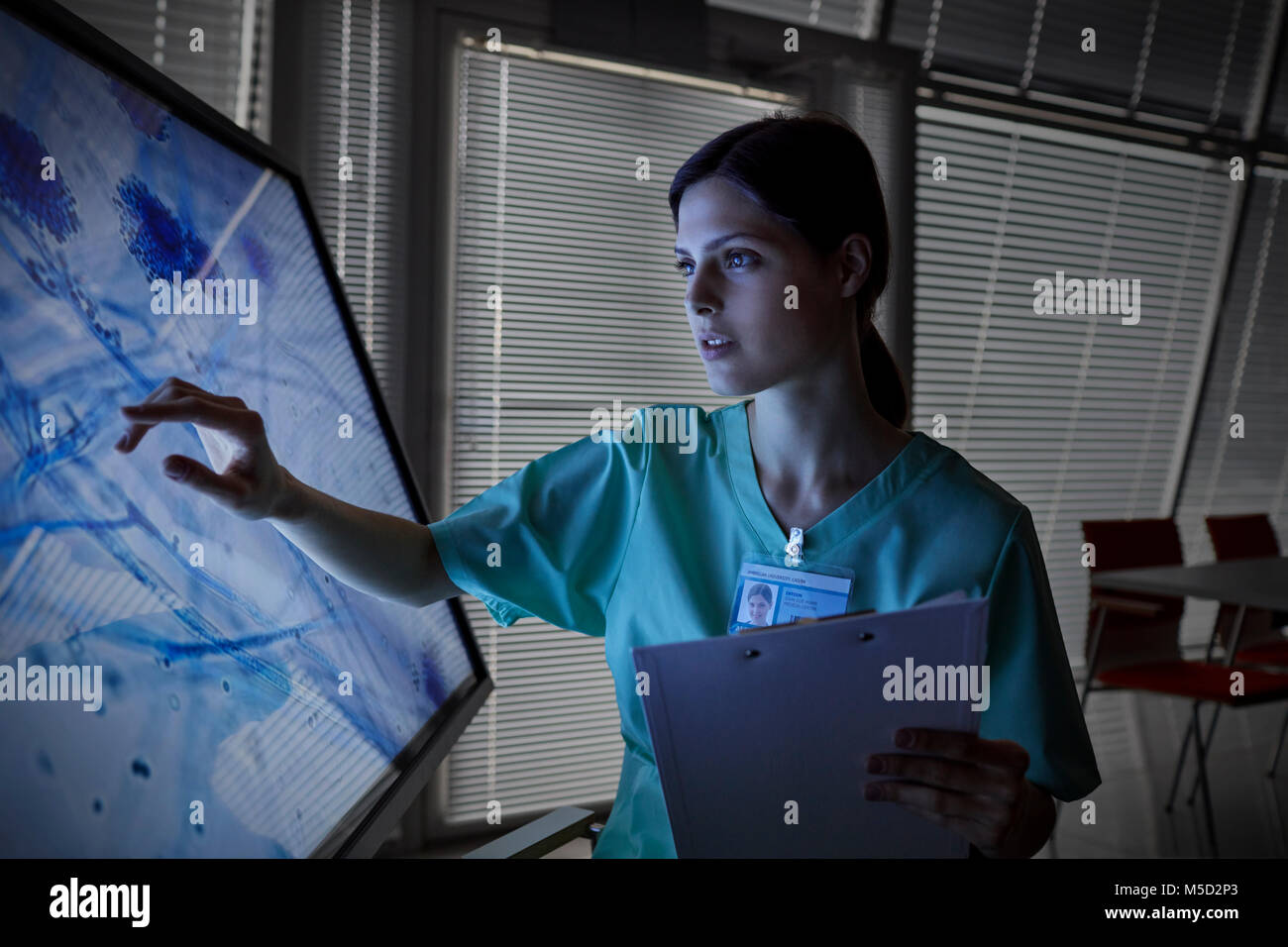 Ernsthafte weibliche Krankenschwester, die den Touchscreen Computer überwachen, Anzeigen von Mikroskop-objektträgern Stockfoto