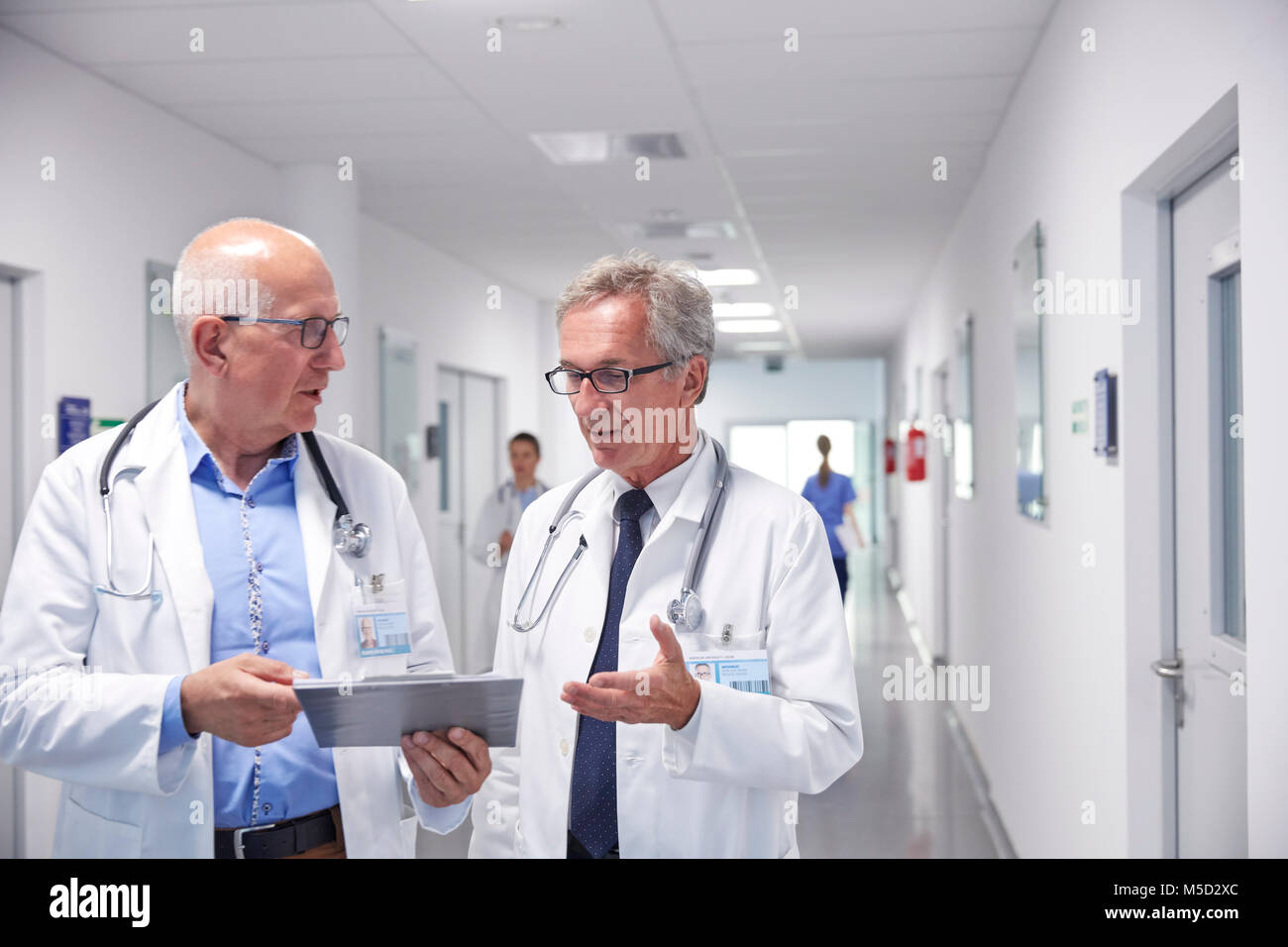 Männliche Ärzte mit Zwischenablage Umläufe bilden, sprechen im Krankenhaus Flur Stockfoto