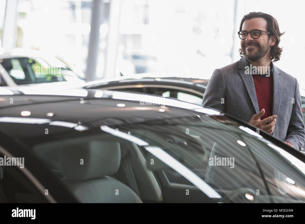 Lächelnd mann Browsen mit neuen Autos in Auto Dealership showroom Stockfoto