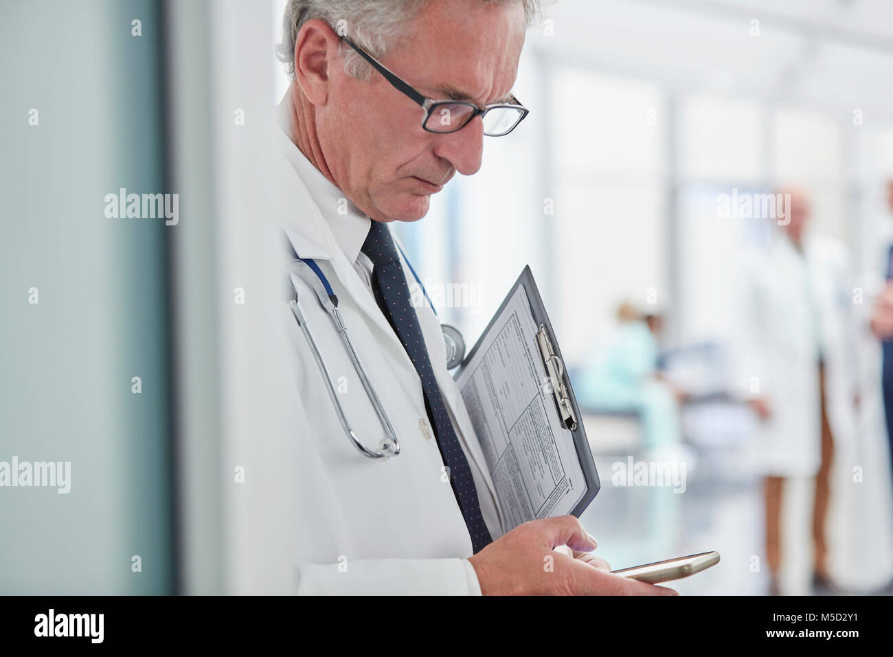 Männlicher Arzt mit Zwischenablage texting mit Smart Phone im Krankenhaus Stockfoto