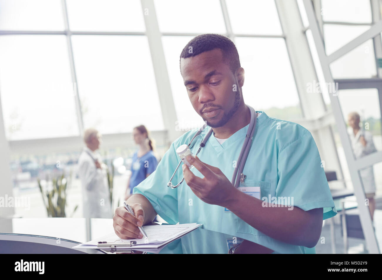 Männliche Krankenschwester mit Zwischenablage Prüfung Medizin Flasche im Krankenhaus Lobby Stockfoto