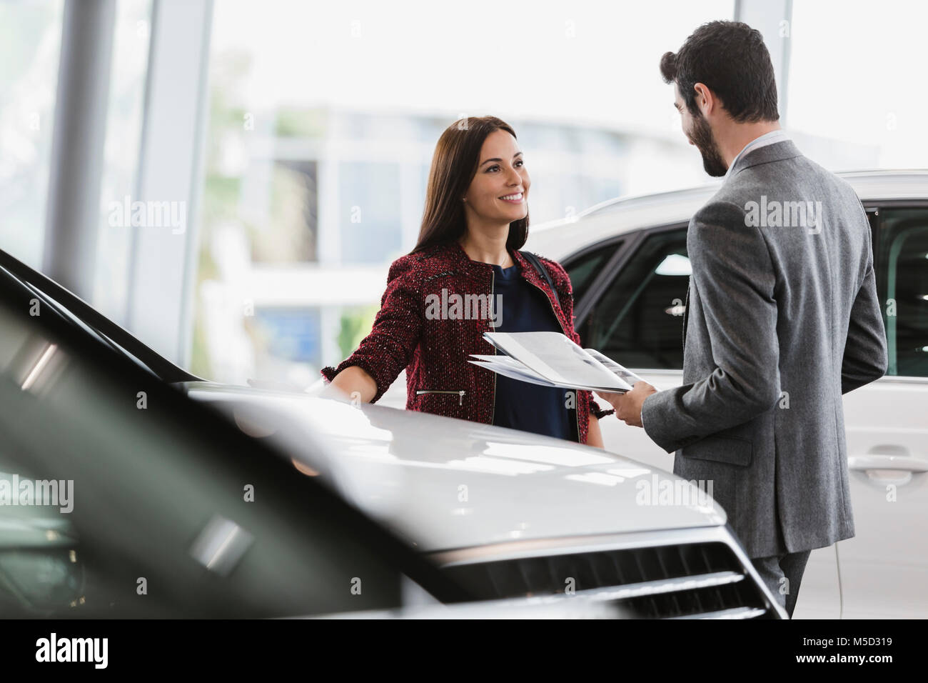 Auto Verkäuferin, die Broschüre zu den männlichen Kunden in Auto Dealership showroom Stockfoto