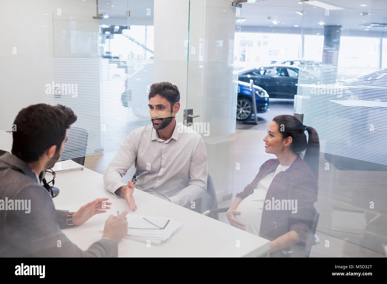 Schwangeren Paare sprechen mit Autoverkäufer, ueber finanzielle Unterlagen in Autohaus Büro Stockfoto