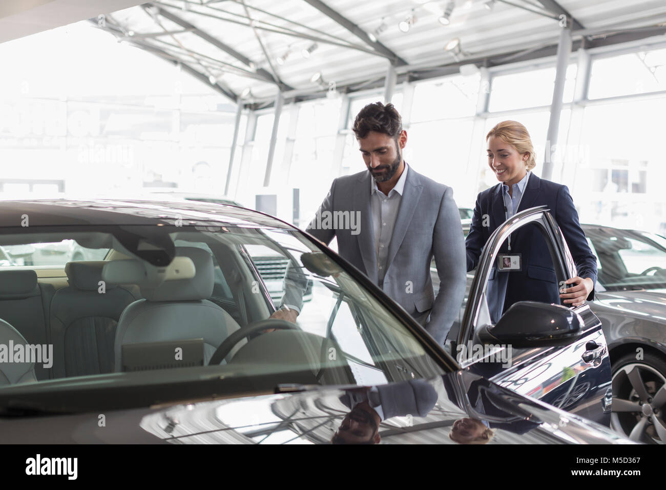 Auto Verkäuferin zeigt neue Auto zu männlichen Kunden in Auto Dealership showroom Stockfoto