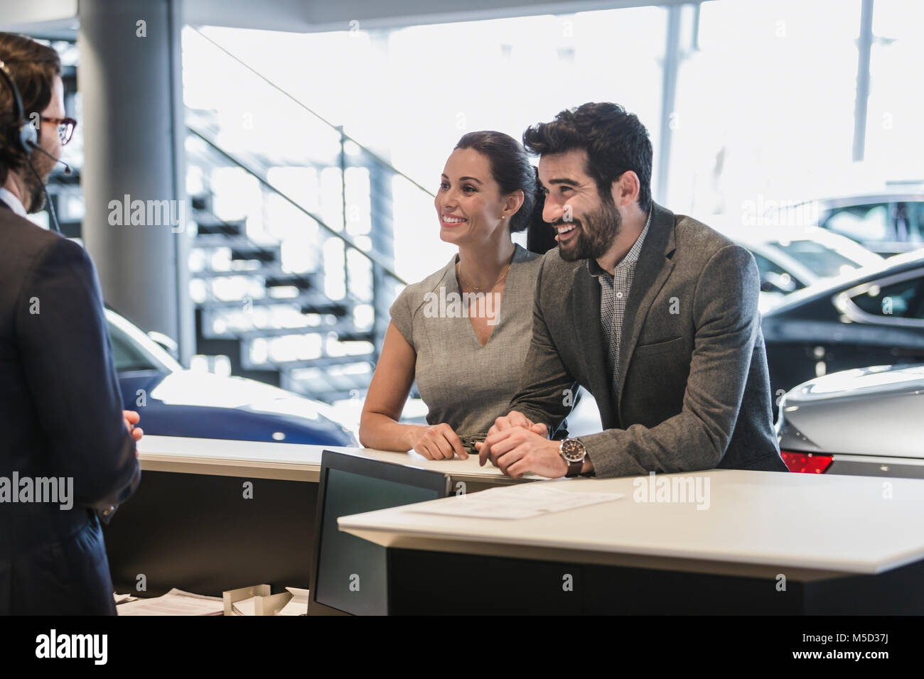 Paar Kunden sprechen über die Angestellte an der Rezeption am Schreibtisch in Auto Dealership showroom Stockfoto