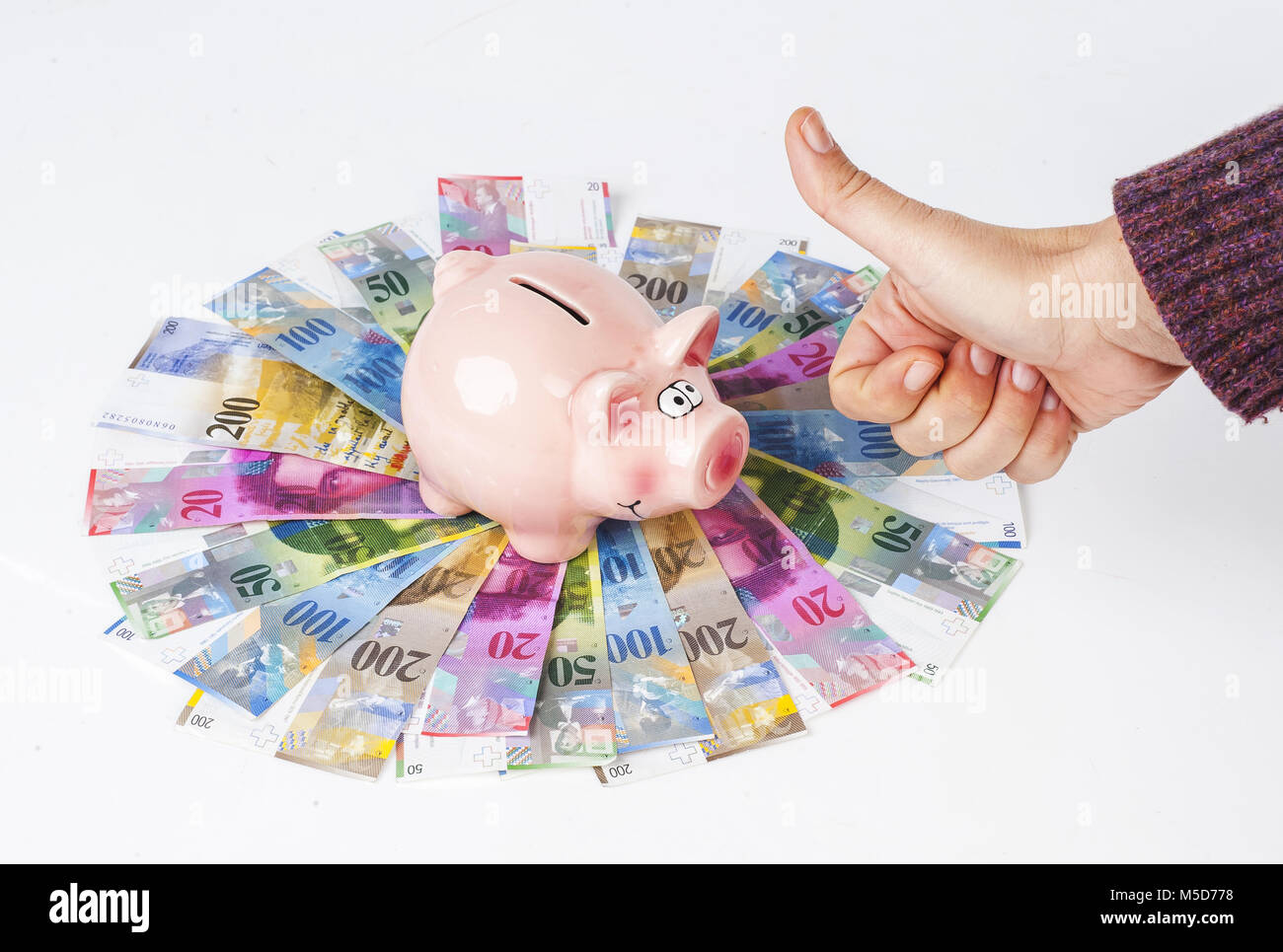 Schweizer Franken Sparschwein und weibliche Hand mit Daumen nach oben Zeichen gegen Stockfoto