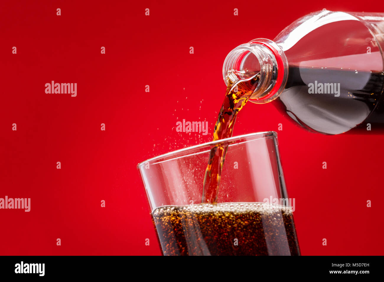 Gießen Erfrischende zuckerhaltigen Softdrink aus einer Flasche in ein Glas auf rotem Hintergrund Stockfoto