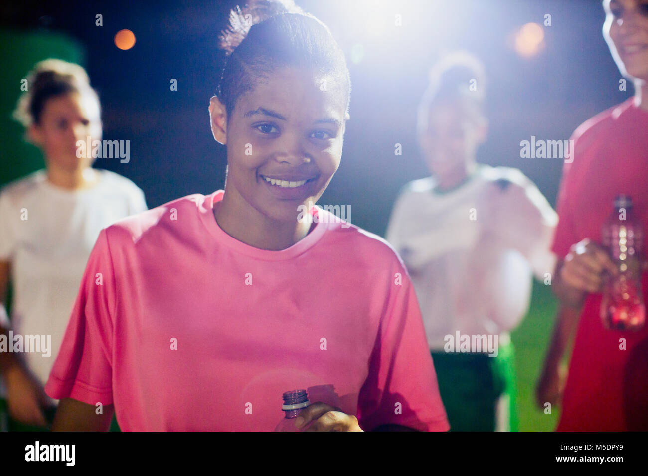 Portrait selbstbewussten jungen weiblichen Fußball-Spieler auf dem Feld mit Mannschaftskameraden in der Nacht Stockfoto