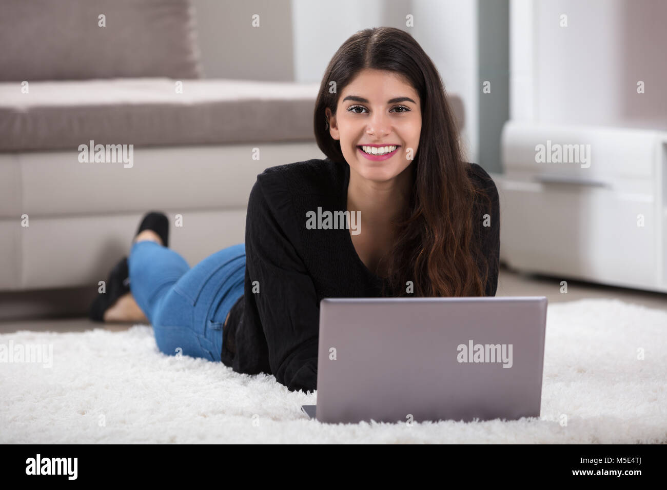 Nahaufnahme einer Lächelnden jungen Frau liegen auf einem weichen Teppich mit Laptop zu Hause Stockfoto