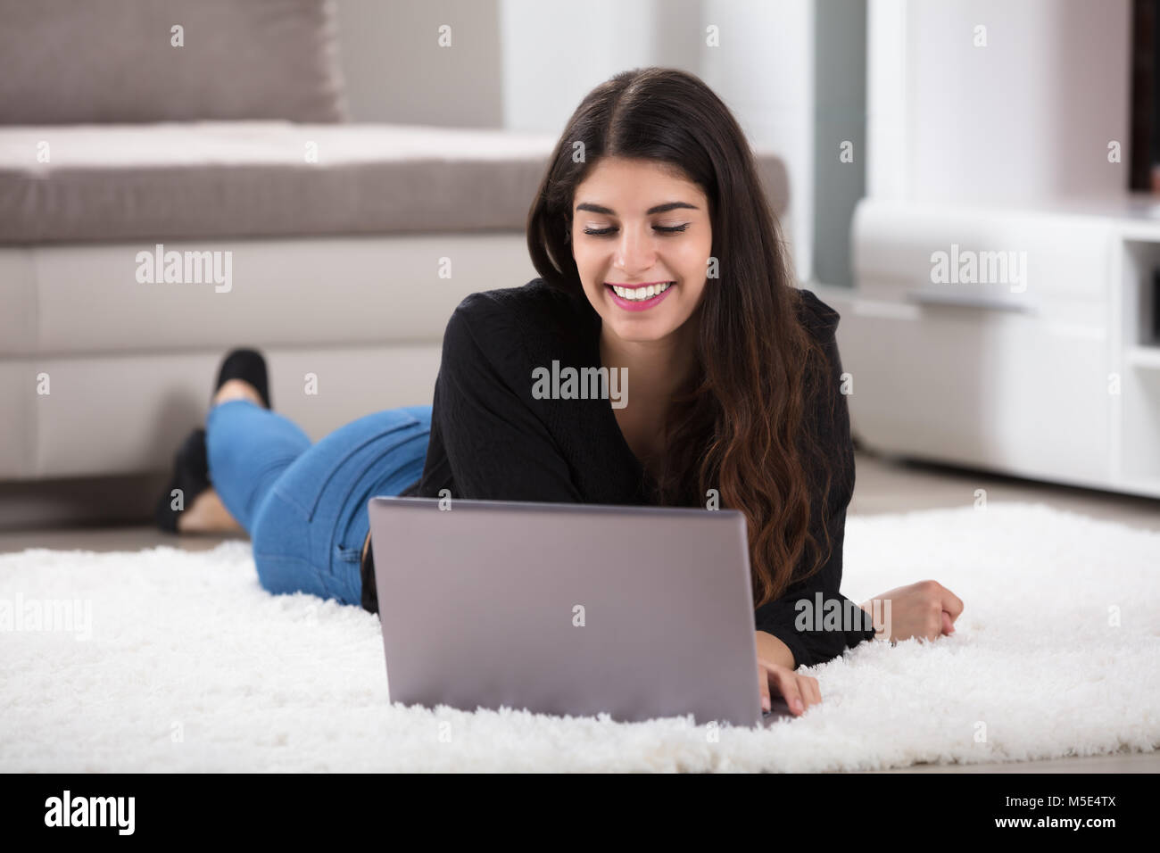 Nahaufnahme einer Lächelnden jungen Frau liegen auf einem weichen Teppich mit Laptop zu Hause Stockfoto