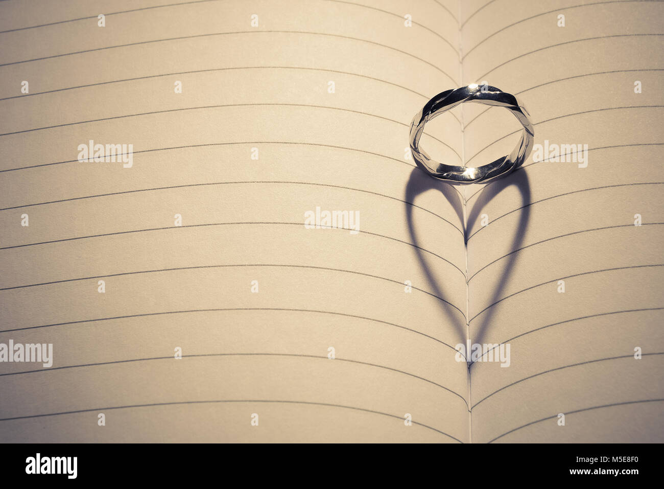 Hochzeit Ring in der Mitte des leeren Notebooks angebracht. Zurück leichte Formen Herzform Schatten. Platz für Kopieren. Liebe und Ehe Konzepte. Stockfoto