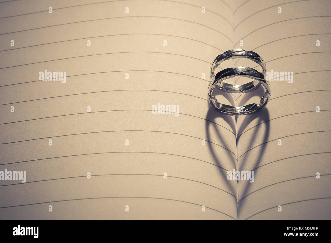 Hochzeit Ringe in der Mitte des leeren Notebooks angebracht. Zurück leichte Formen Herzform Schatten. Platz für Kopieren. Liebe und Ehe Konzepte. Stockfoto
