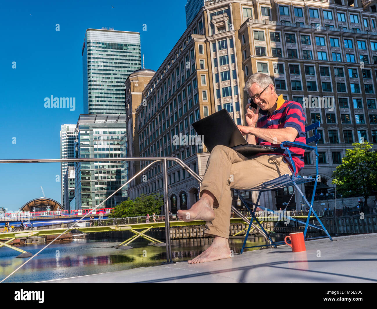 Entspannt reife selbständige Unternehmer auf seinem Büro Boot sprechen auf dem iPhone Smartphone arbeiten an einem Laptop Canary Wharf London E14 Stockfoto