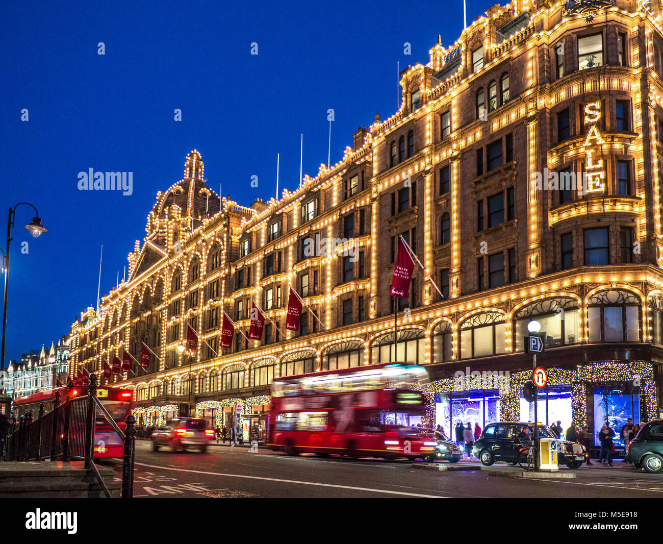 Harrods Sale Lights Dämmerung Kaufhaus beleuchtet in der Nacht mit 'Sale' Schild Käufer rote Busse und vorbei an Taxis auf der ULEZ Route Knightsbridge London SW1 Stockfoto