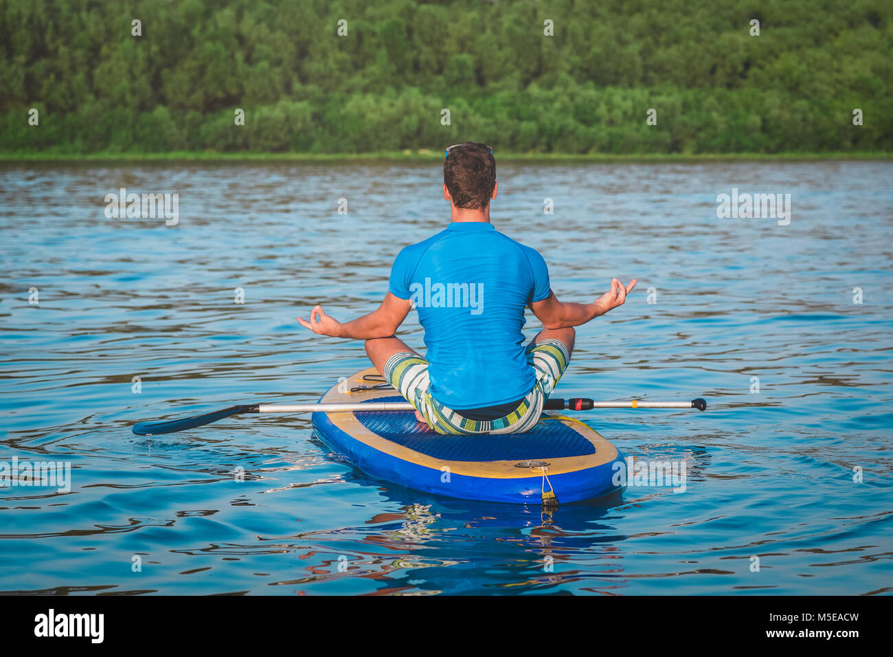 Rückansicht des Menschen Yoga auf dem sup Board mit Paddeln. Meditative Lotussitz Stockfoto